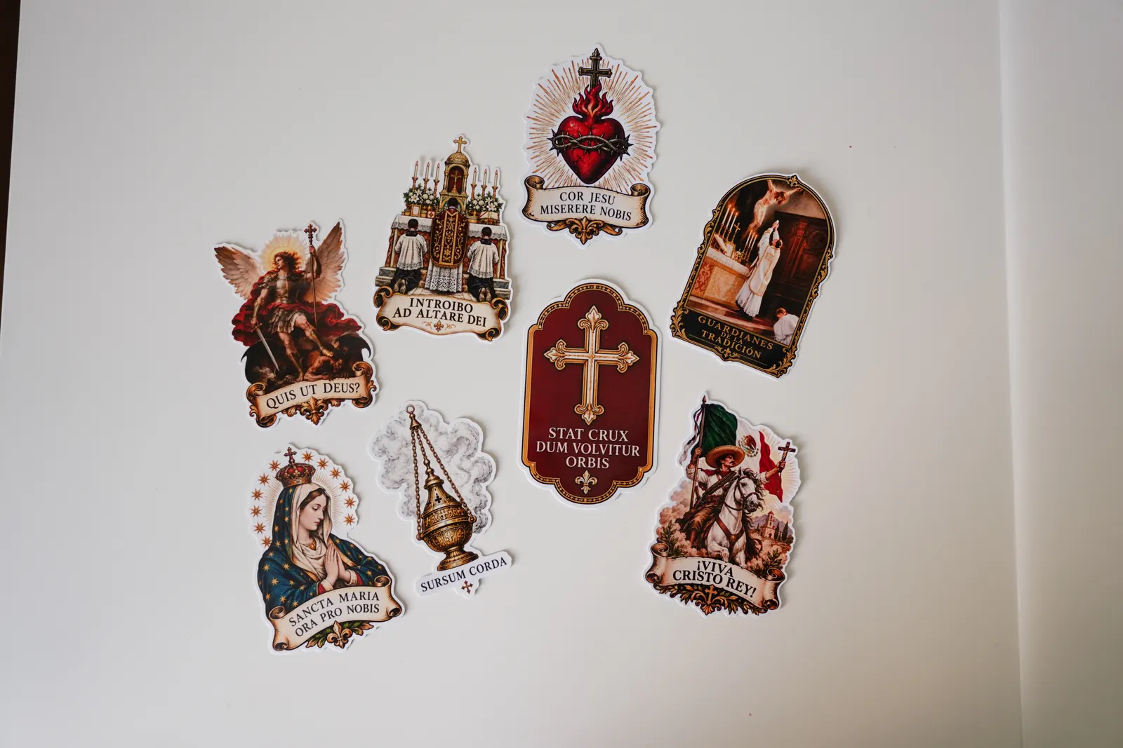Ocho stickers de vinil troquelados de arte sacro con leyendas en latín sobre una mesa blanca