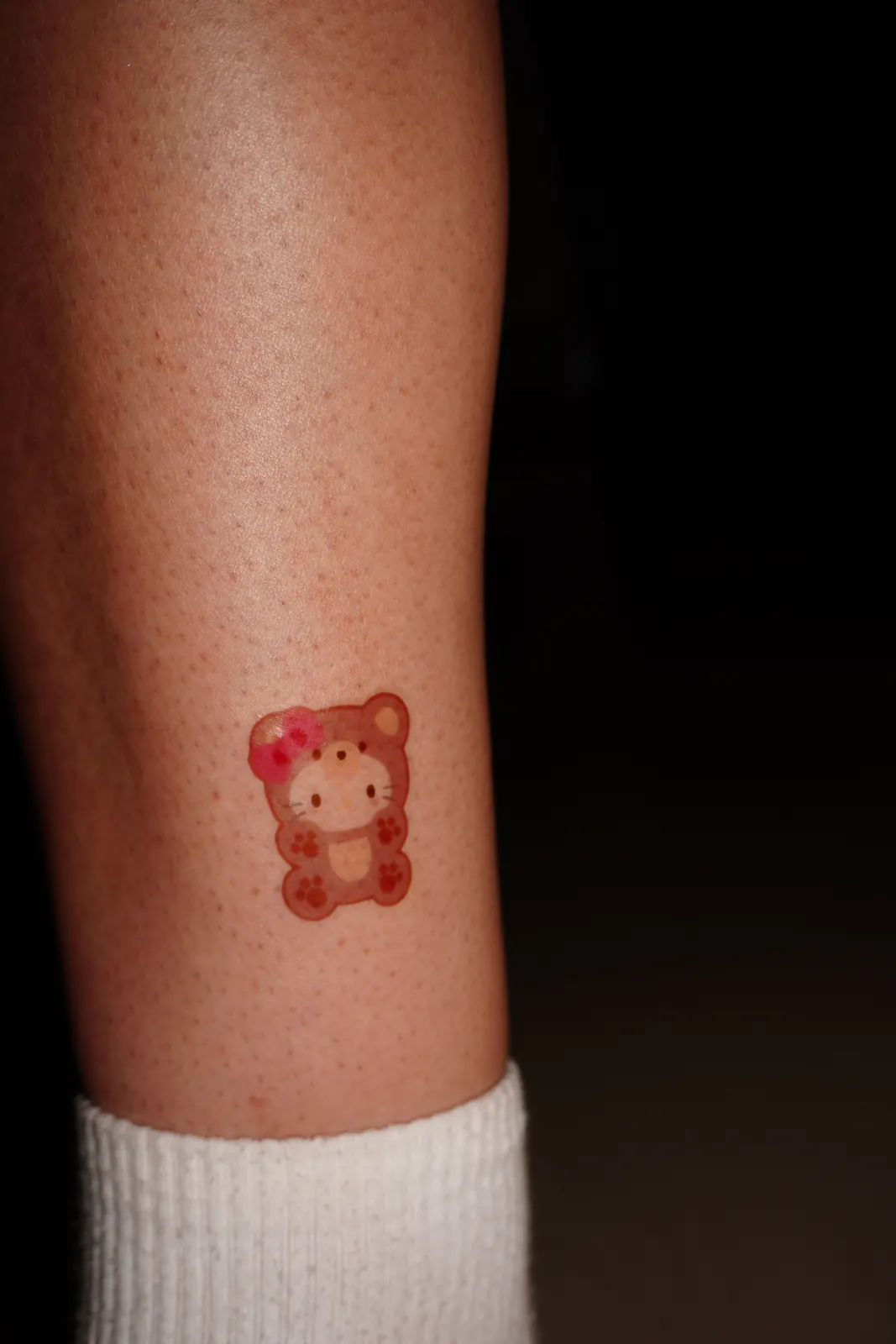 Hello Kitty in a bear costume with a pink bow as a temporary tattoo on the leg